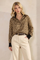 Model wearing a Leopard Print Satin Blouse with long sleeves and black cuffs, styled with high-waisted cream trousers and a brown belt, showcasing a timeless capsule wardrobe piece.