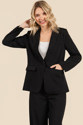 Woman smiling wearing The Worth Blazer Black, styled with a white top underneath, showcasing a clean, timeless design perfect for a versatile capsule wardrobe.