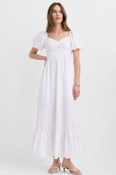 Woman wearing The Belle Maxi Dress in white with puffed sleeves and a ruched neckline, showcasing a stretchable, timeless minimalist design ideal for modern capsule wardrobes.