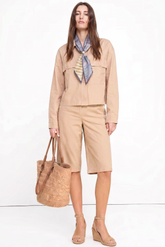 Woman wearing The Sahara Linen Set in a neutral beige tone, styled with a patterned scarf, woven tote bag, and wedge sandals, showcasing a timeless minimalist capsule wardrobe piece.