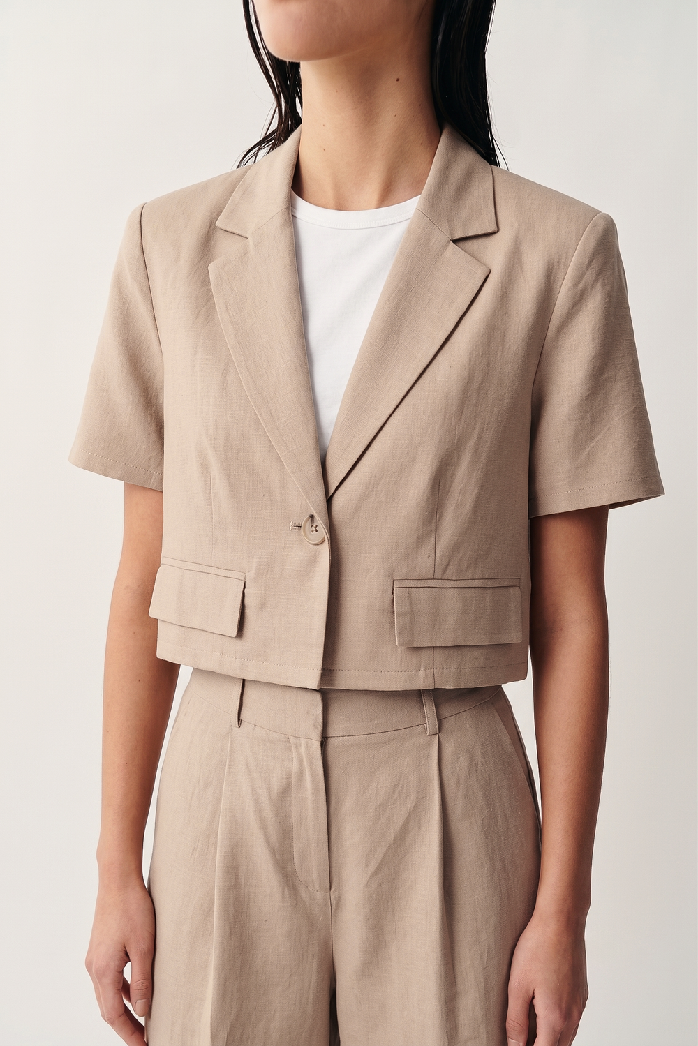 Model wearing the Riviera Linen Tailored Blazer-Khaki with short sleeves, single button closure, notch lapels, and front flap pockets, styled with matching high-waist linen trousers.