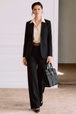 Model wearing The Worth Avenue Trousers in a clean, tailored black fit paired with a cream blouse, black blazer, brown belt, and structured black handbag, showcasing timeless minimalism and refined capsule wardrobe style.