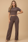 Woman wearing The Siena Lounge Set in a soft, ribbed brown fabric featuring a short-sleeve cropped top and high-waisted wide-leg pants, styled for a timeless, minimalist capsule wardrobe.