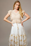 Woman wearing The Coco Palm Dress, featuring a white tiered skirt with gold palm prints and a beige knit top with ruffled sleeves, embodying timeless minimalism and curated style.