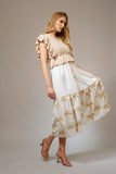 Woman wearing The Coco Palm Dress featuring a white flowing skirt with subtle palm tree patterns, styled with a beige textured ruffle top and strappy heels, embodying timeless minimalism.