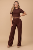 A woman wearing The Siena Lounge Set in a rich burgundy color, featuring a ribbed short-sleeve crop top and matching high-waisted wide-leg pants, styled with minimal accessories against a neutral background.