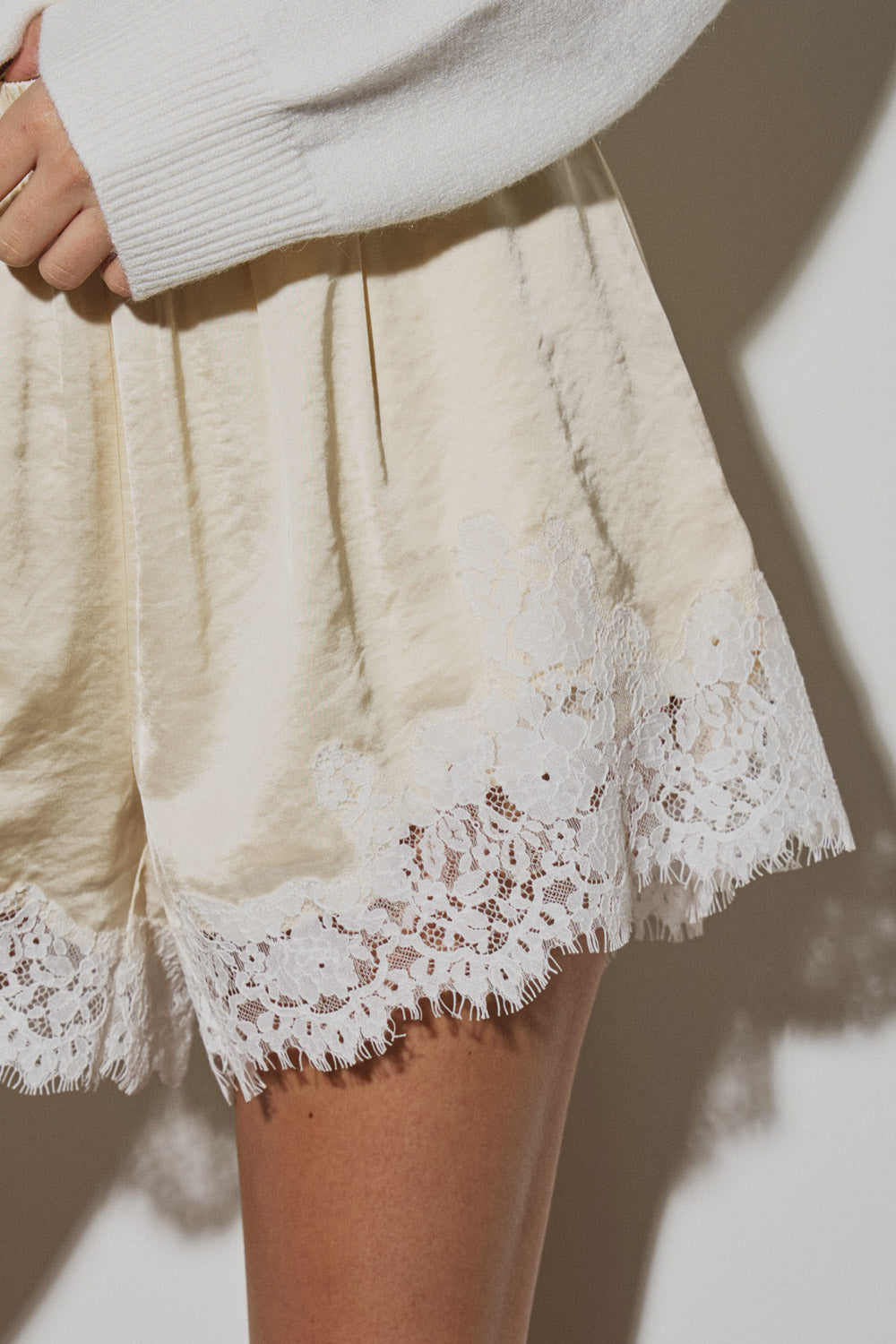Close-up of a model wearing The Camille Lace Satin Short in cream with delicate white lace trim, showcasing a stretchable satin fabric and clean, timeless design.