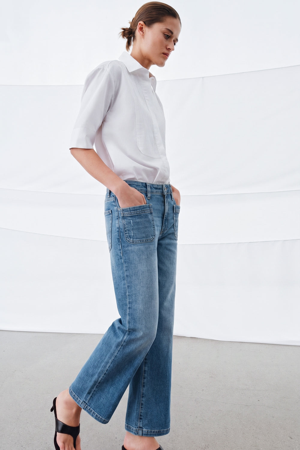 Woman wearing a white blouse paired with light blue denim Camden Ankle Jean, featuring a relaxed straight-leg fit and front patch pockets, styled with black sandals.