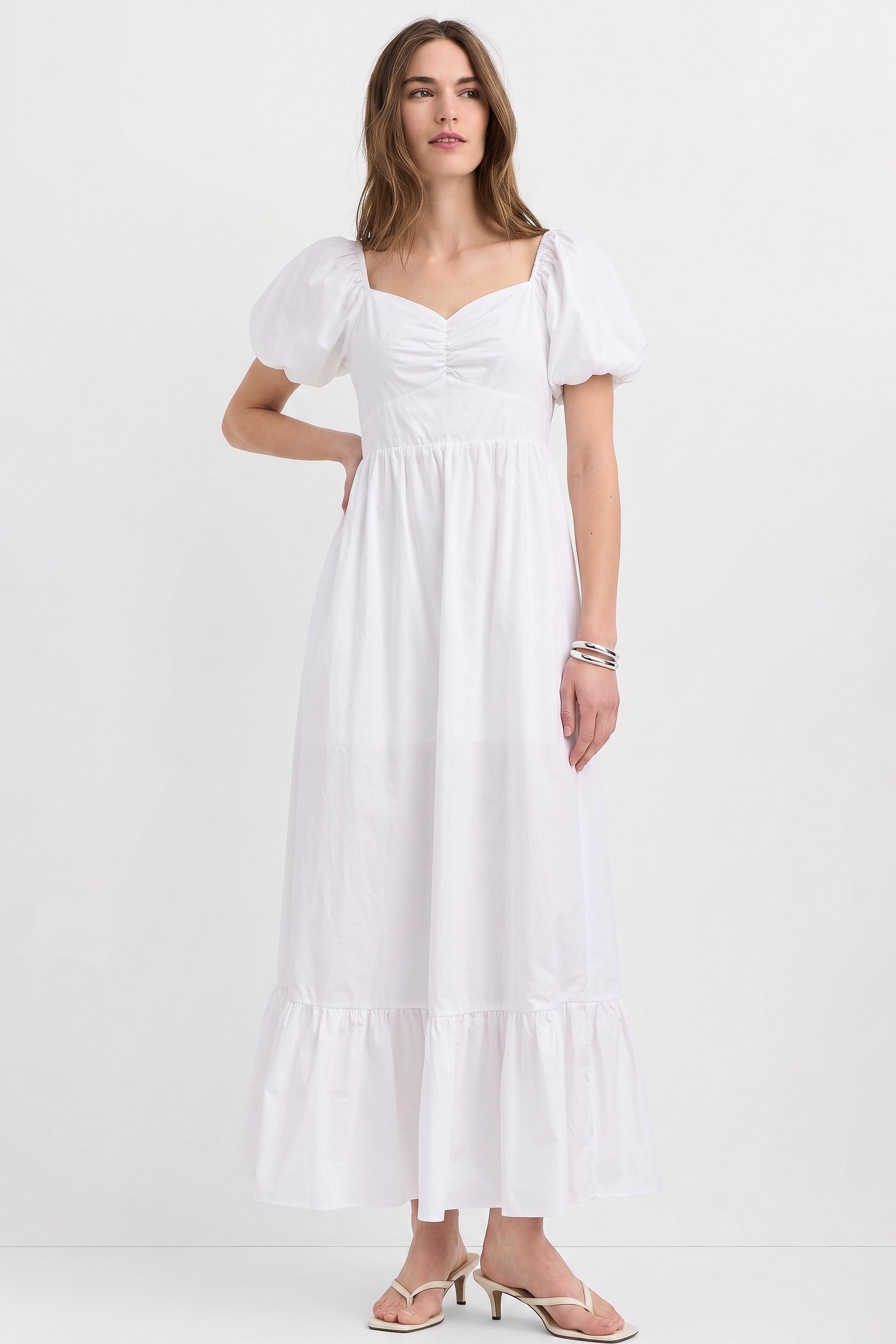 Woman wearing The Belle Maxi Dress in white with puffed sleeves and a ruched neckline, showcasing a stretchable, timeless minimalist design ideal for modern capsule wardrobes.
