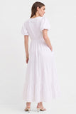 Woman wearing The Belle Maxi Dress in white, featuring puff sleeves, a gathered waist, stretchable fabric, and a flowing tiered hem, styled with minimalist heels.
