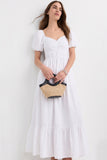 Woman wearing The Belle Maxi Dress in white with puff sleeves and a gathered bodice, holding a small straw handbag with black handles, styled for a timeless capsule wardrobe look.