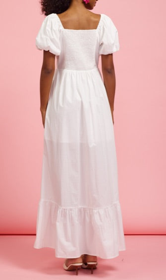 A back view of a model wearing The Belle Maxi Dress, featuring a stretchable bodice with puff sleeves and a flowing, tiered skirt in timeless white, perfect for a curated capsule wardrobe.