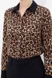 Close-up of a Leopard Print Satin Blouse featuring a smooth, glossy fabric with bold leopard spots and a contrasting black collar and cuffs, styled with tailored black trousers.