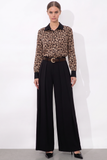 Woman wearing a Leopard Print Satin Blouse with long sleeves and a black collar, tucked into high-waisted black wide-leg trousers with a belt, styled for a modern, refined look.