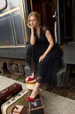 Orient Express Black Lace Maxi Dress – Whimsigoth Holiday & NYE Gown worn with red bow heels beside vintage luggage on a classic train platform