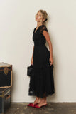 Orient Express Black Lace Maxi Dress – Whimsigoth Holiday & NYE Gown shown on a woman with layered lace skirt, cap sleeves, and red heels beside vintage trunks