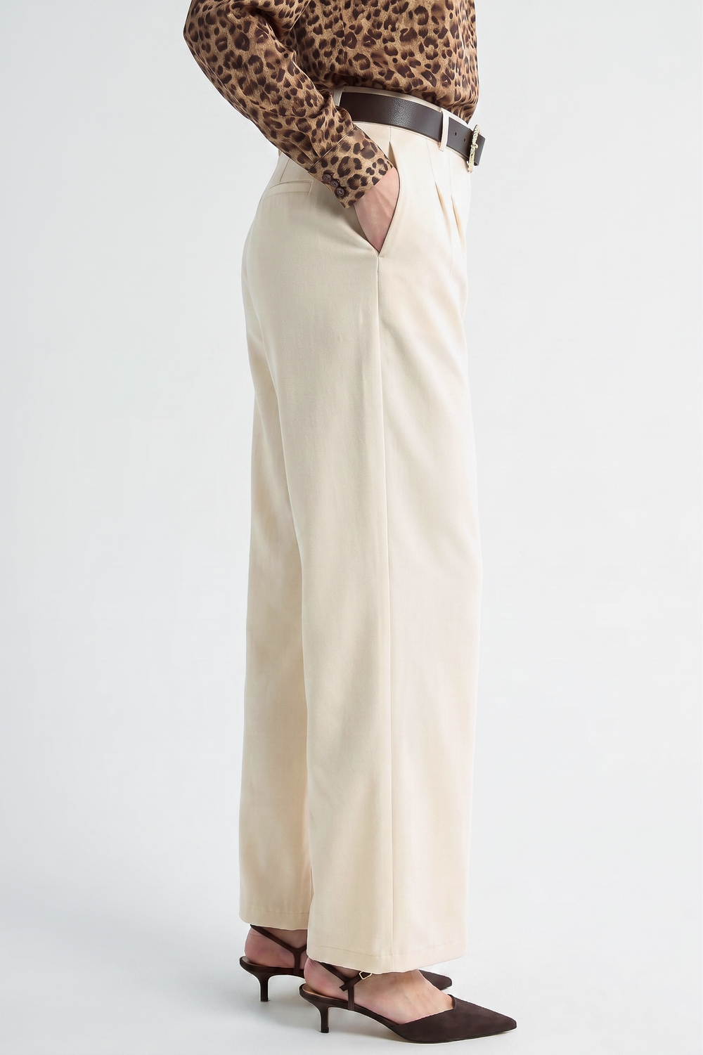 Side view of a model wearing Oyster Belted Wide Leg Trousers in a neutral tone, styled with a dark belt, leopard print blouse, and pointed-toe heels, showcasing a clean and timeless silhouette.