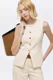 Woman wearing The Oyster Longline Vest in a neutral cream tone with gold buttons, styled with matching pants and carrying a brown tote bag, showcasing a minimalist, timeless capsule wardrobe piece.
