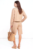 A woman seen from behind wearing The Sahara Linen Set, featuring a tailored linen jacket and knee-length shorts in a neutral beige tone, paired with a woven straw tote and beige wedge sandals for a timeless, minimalist look.