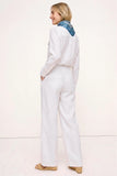 Back view of a woman wearing The Santorini Linen Shirt – Ivory paired with matching linen pants and a blue patterned scarf, showcasing a clean, timeless capsule wardrobe look.