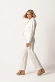 Woman walking confidently wearing The Santorini Linen Shirt – Ivory paired with matching ivory pants and beige wedge sandals, showcasing timeless minimalism and versatile style.