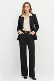 Woman wearing The Worth Blazer Black with a cream blouse, black tailored pants, and black heels, styled for a timeless, minimalist, and modern workwear look.