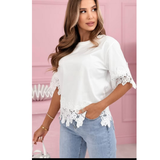 Woman wearing The Harper Lace Tee – White with stretchable fabric, featuring delicate lace trim on sleeves and hem, styled with light denim jeans against a pink background.
