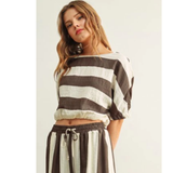 A model wearing The Miou Muse Boat Neck Stripe Top featuring wide horizontal stripes in neutral tones, showcasing a clean, timeless design perfect for a curated capsule wardrobe.